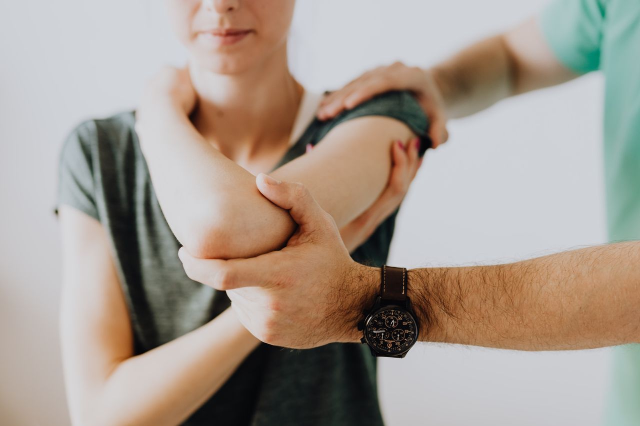 About Crop faceless osteopath in modern wristwatch and uniform bending arm of anonymous thoughtful woman in casual wear in doctor office in hospital